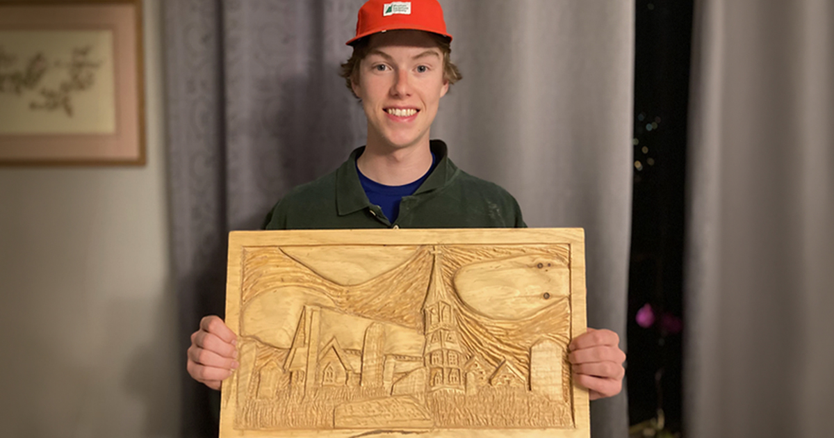 A young man holds up a carving of a church